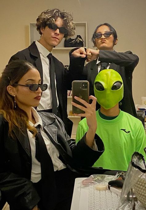 three people dressed up as aliens and one is taking a selfie with a cell phone