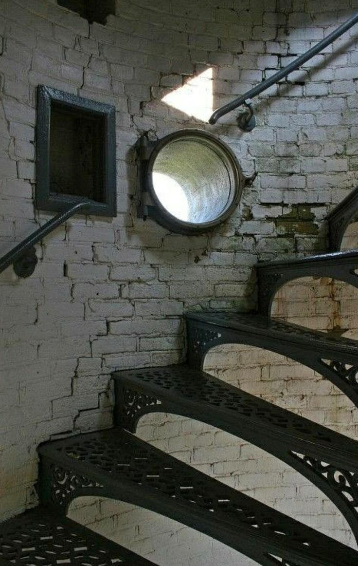 an old set of stairs with a round mirror on the wall above it, in front of a brick wall