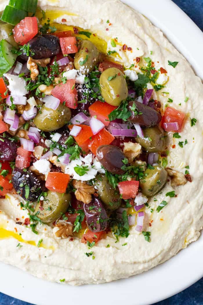 hummus with olives, tomatoes, onions and feta cheese on top in a white bowl