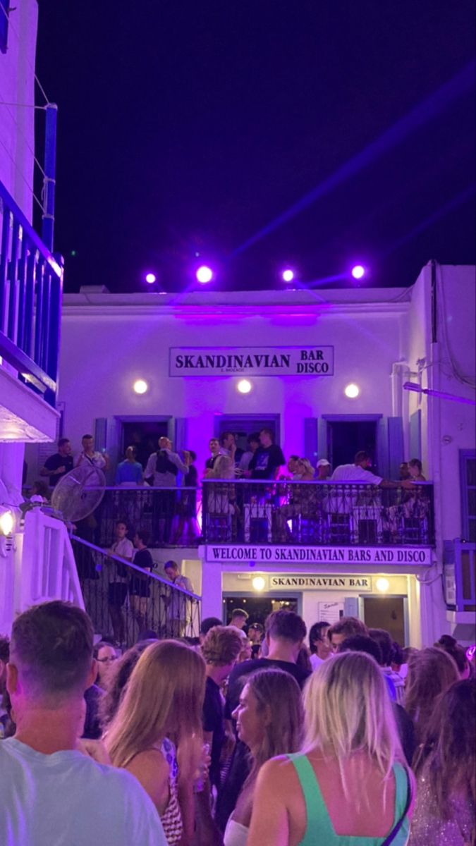 a crowd of people standing in front of a white building with purple lights on it