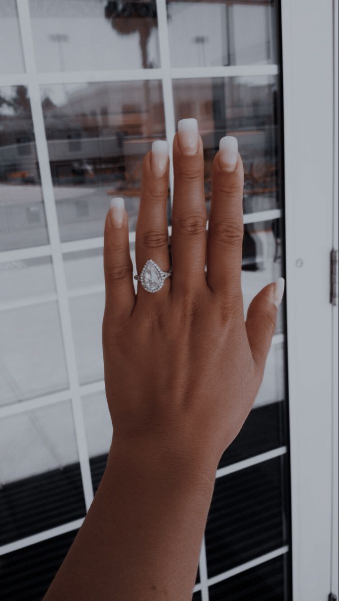 a woman's hand with a diamond ring on her left thumb, in front of a glass door