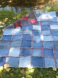 an old patchwork quilt laying on the grass next to a pond with leaves around it