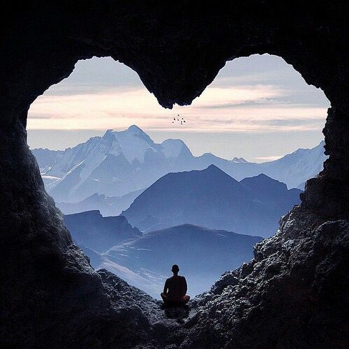 a man sitting in the middle of a cave looking out at mountains and snow capped peaks