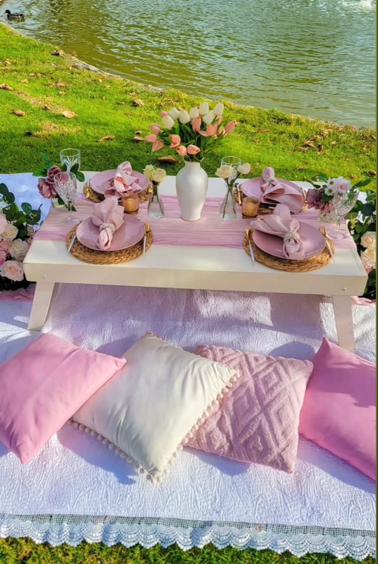 a table with pink and white pillows on top of it next to a body of water