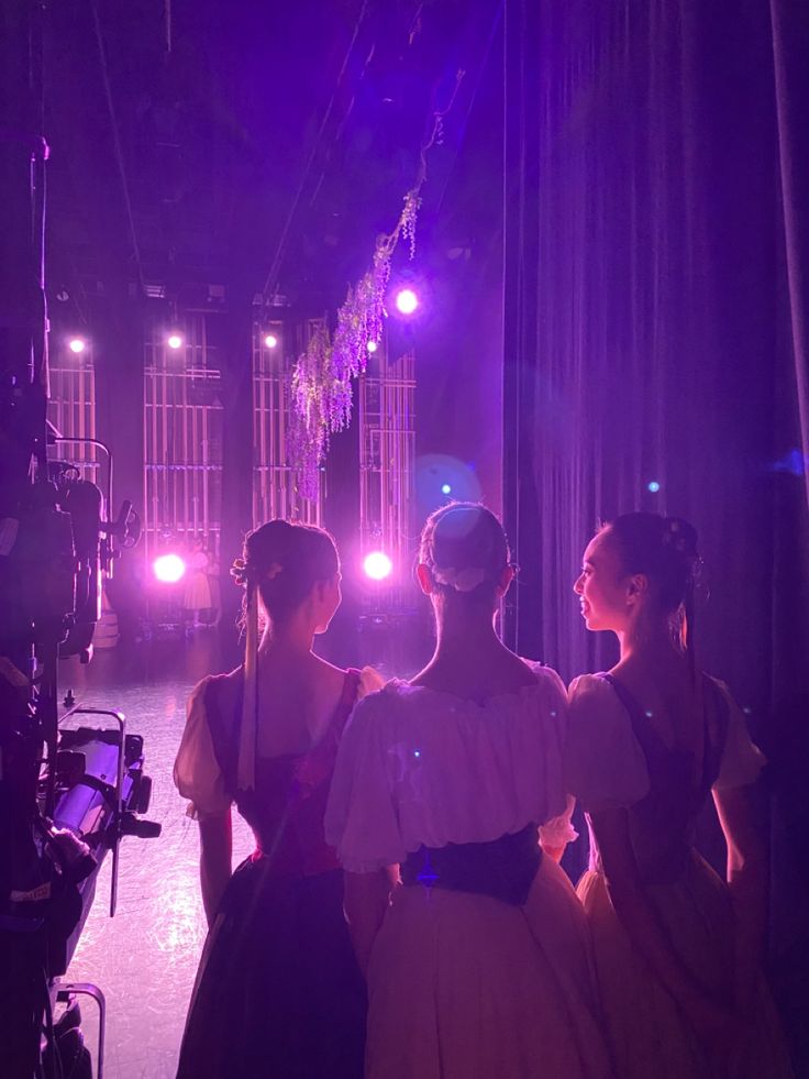 three women in dresses standing next to each other on stage with bright lights behind them