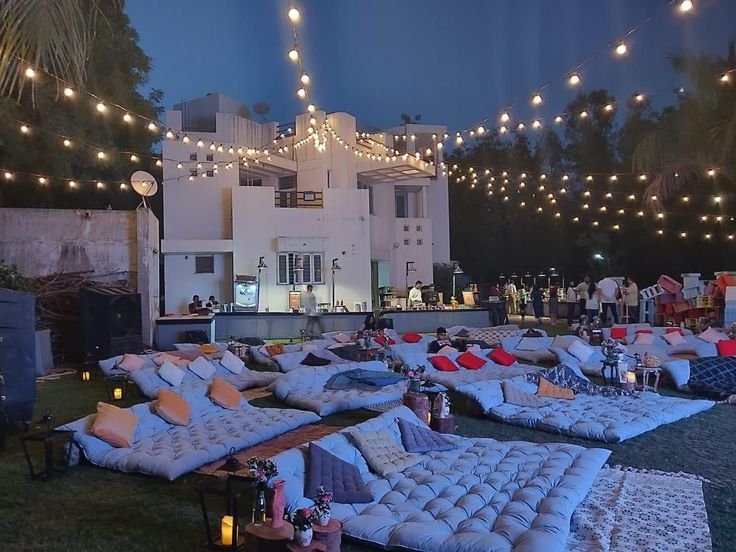 an outdoor party with lots of pillows and lights strung from the ceiling over it's lawn