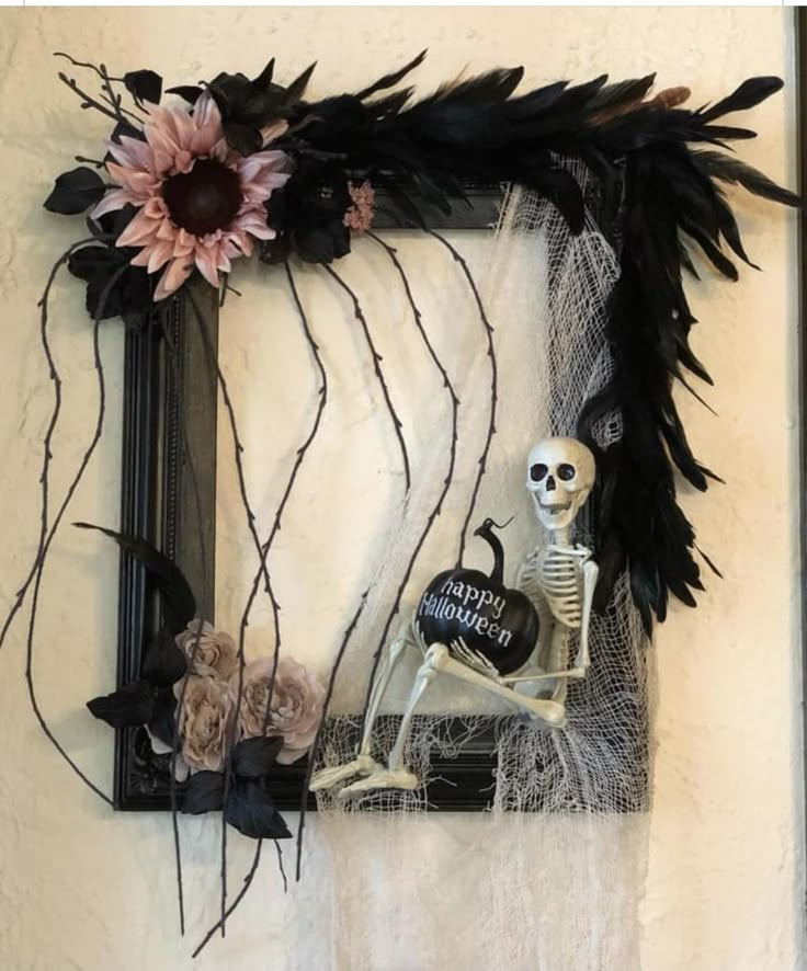 a skeleton sitting in front of a frame with flowers and feathers on it's side