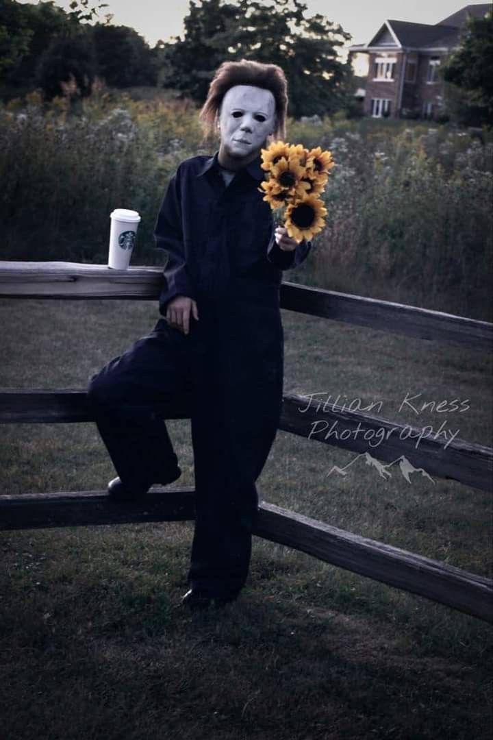 a person with a creepy mask holding sunflowers in front of a wooden fence