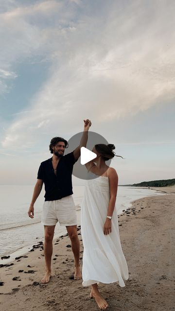 a man and woman standing on top of a beach next to the ocean holding hands