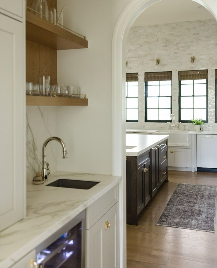 an archway leads into a kitchen with marble counter tops and white cabinets, along with wooden flooring