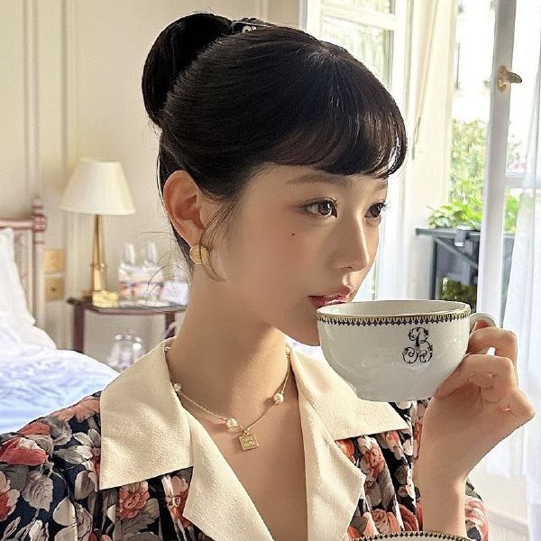 a woman drinking out of a cup while sitting in front of a bed with a window