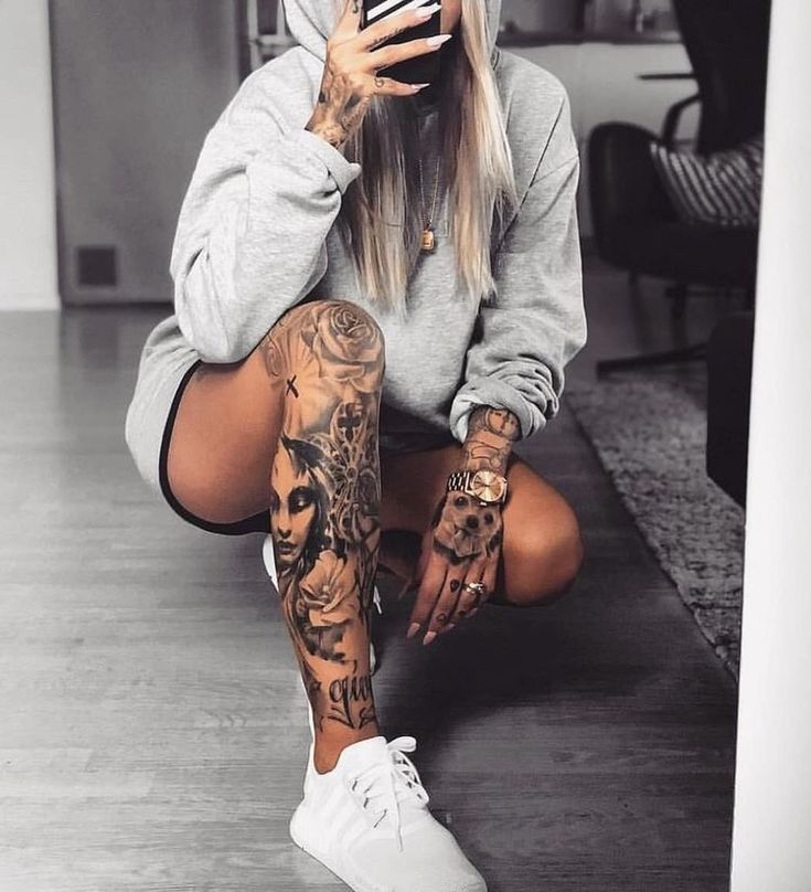 a woman sitting on the floor with tattoos on her arms and legs, holding a cell phone