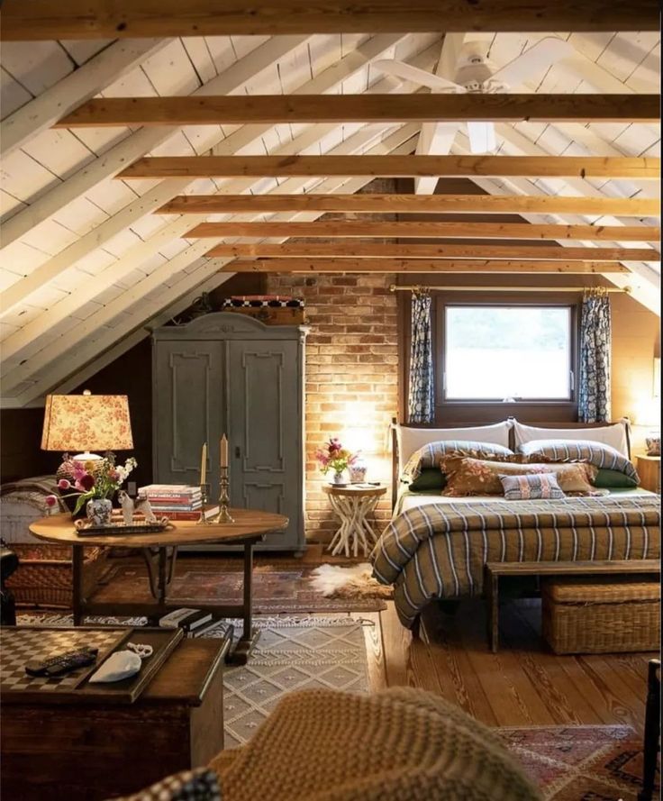 an attic bedroom with exposed wood beams and brick walls, bed in foreground, couch on far side