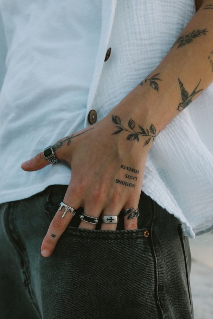 a person with tattoos on their arms and hand holding onto his jeans pocket while wearing a white shirt