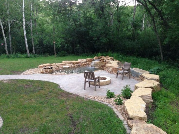 an outdoor fire pit surrounded by rocks and chairs in the middle of a grassy area