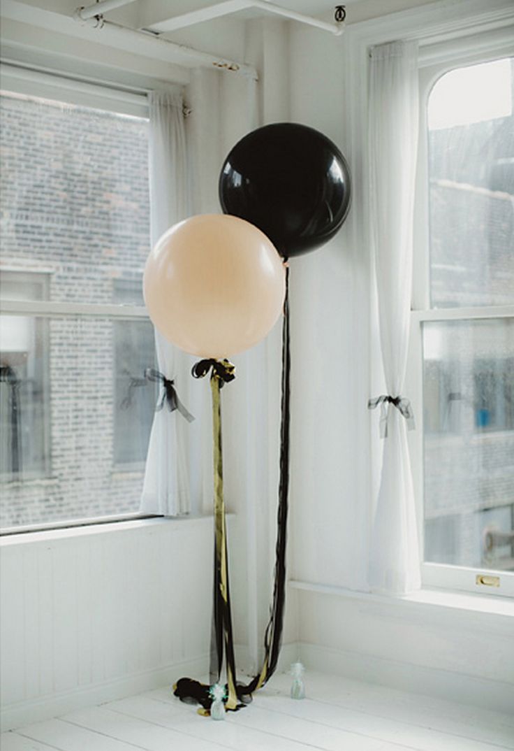 two balloons in the corner of a room with white walls and windows, one black and one pink