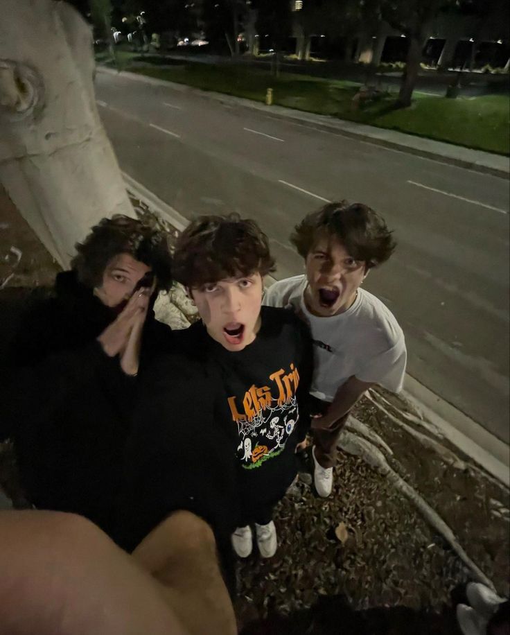 three young men standing next to each other on the side of a road at night