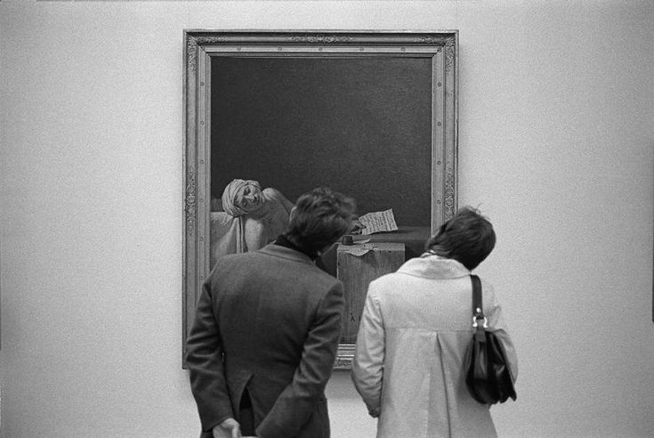 black and white photograph of two people looking at an art work on display in a museum