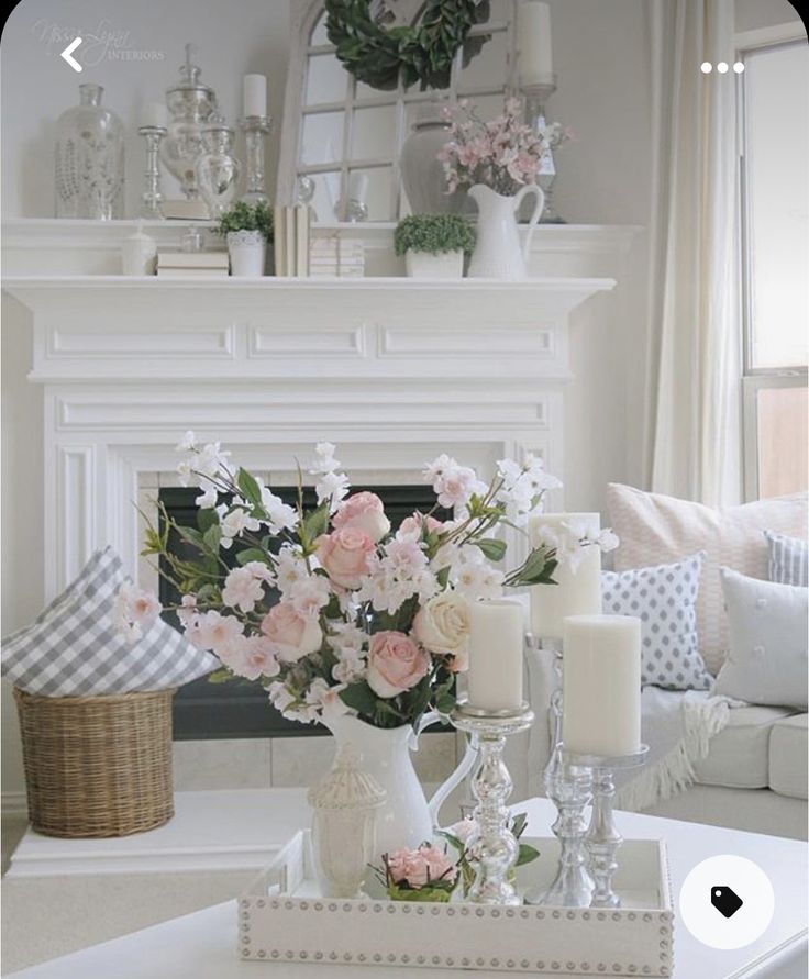 a living room filled with white furniture and flowers on top of a fireplace mantel