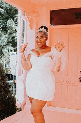 a woman in a short white dress standing on the porch with her hands up and smiling