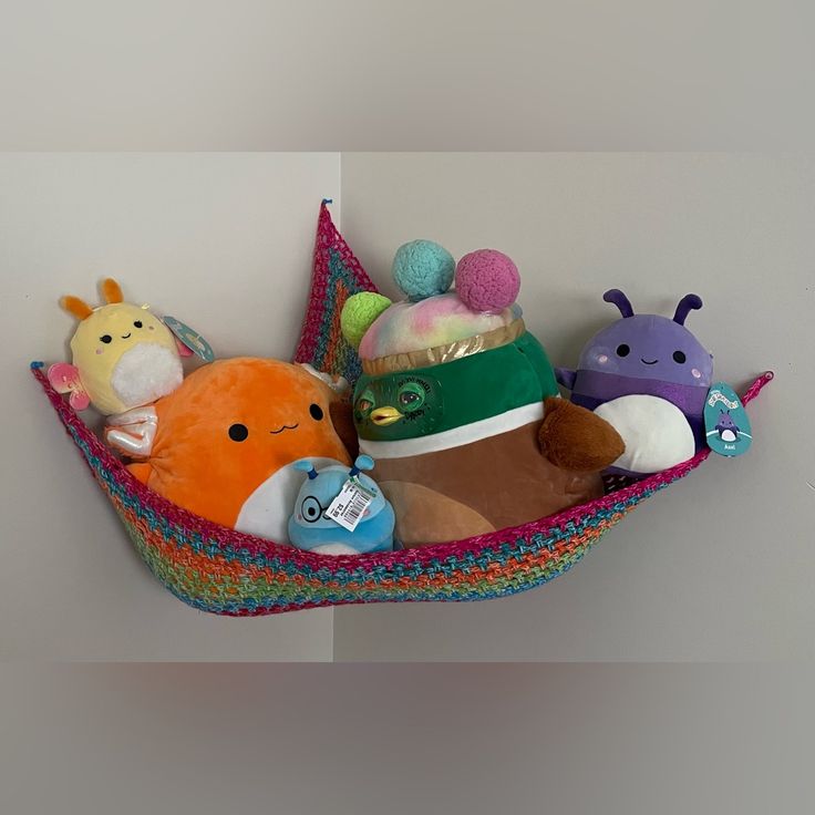 stuffed animals are sitting in a colorful hammock on the wall next to each other