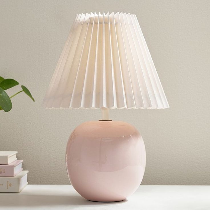 a pink lamp sitting on top of a table next to a book and a potted plant