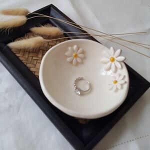 a white bowl sitting on top of a black tray next to some grass and flowers