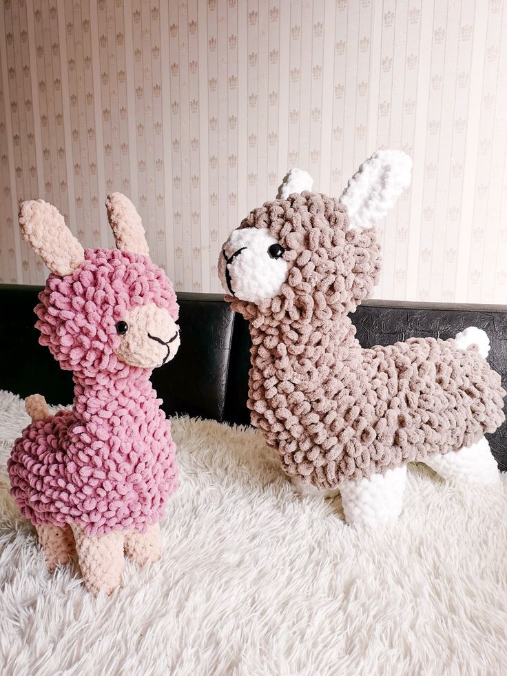 two knitted llamas sitting on top of a white rug next to each other