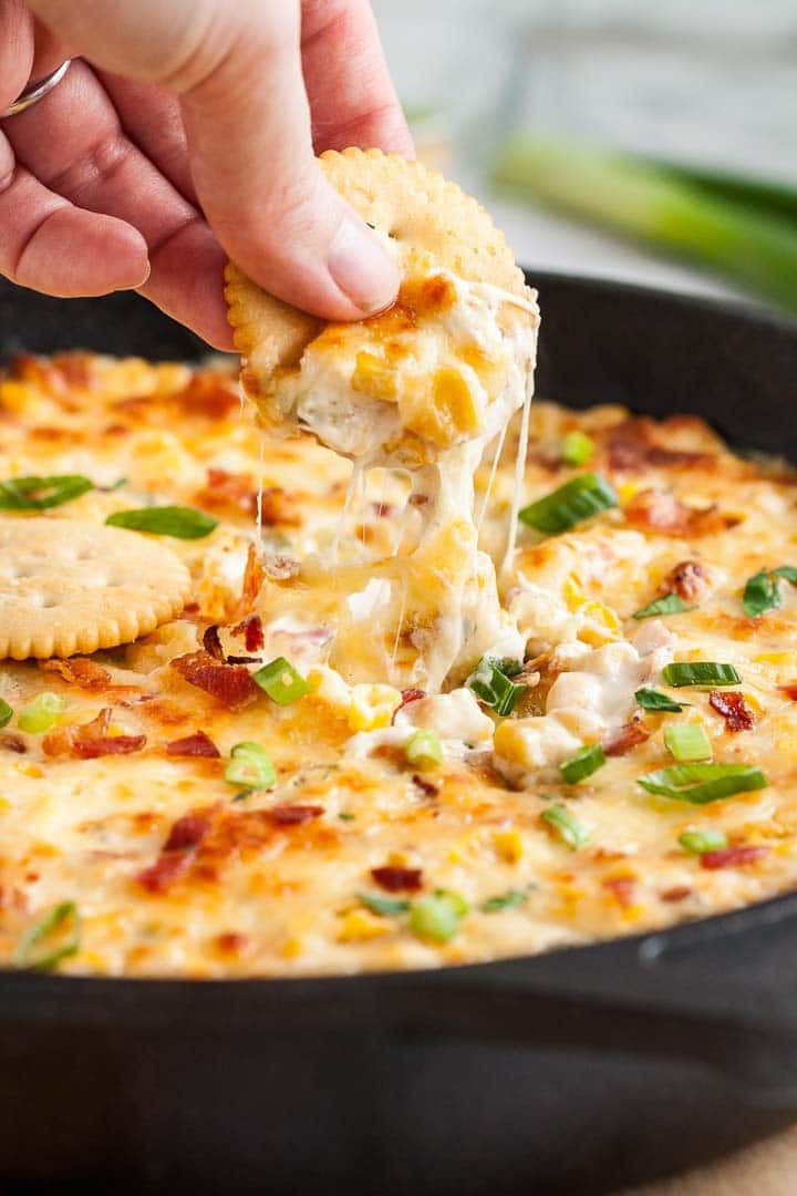 a person dipping some food into a skillet with cheese and green onions on top