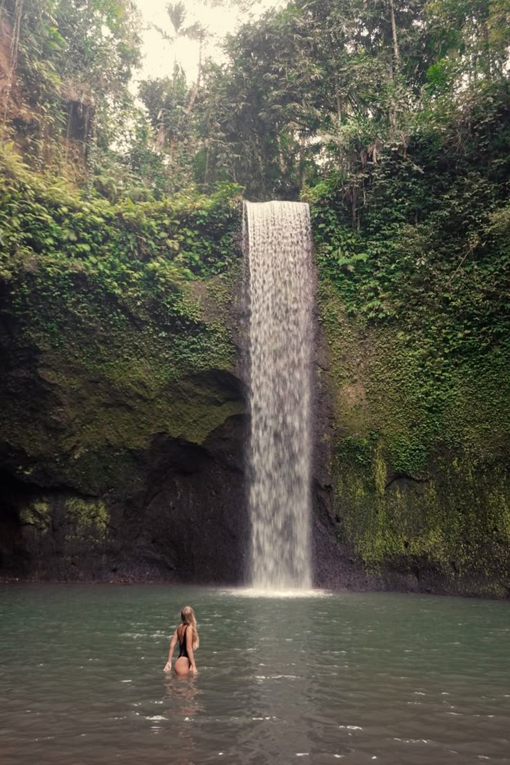 a woman standing in the water next to a waterfall