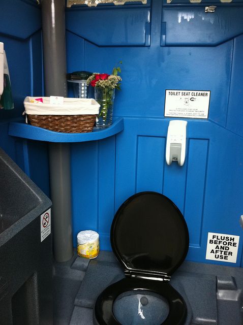 a black toilet sitting in a bathroom next to a blue wall and shelf with flowers on it