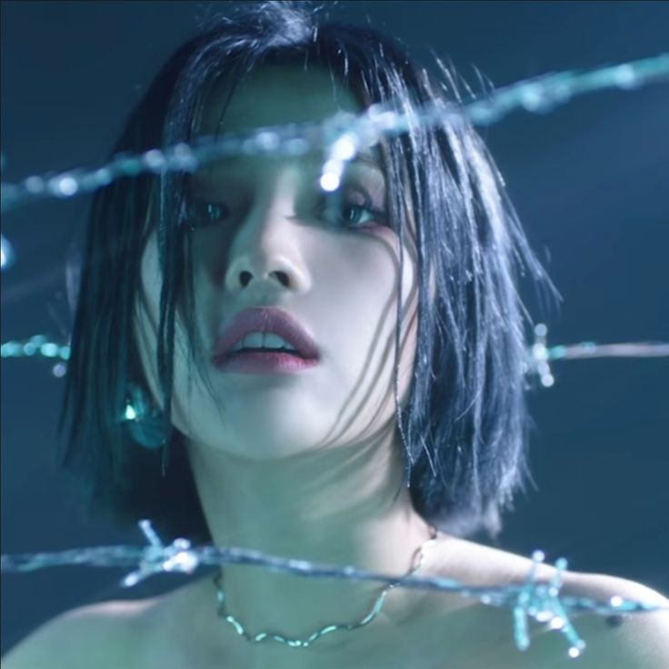 a woman with black hair and blue eyes stares at the camera from behind barbed wire