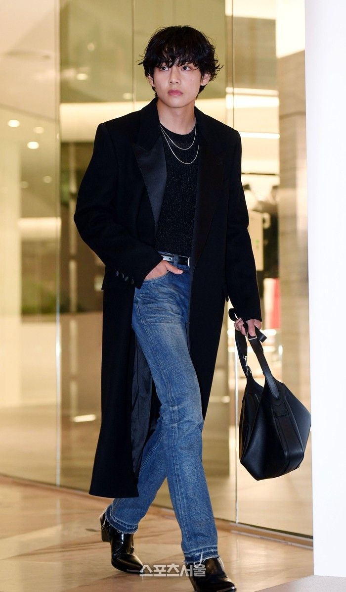 a young man in black coat and jeans carrying a handbag