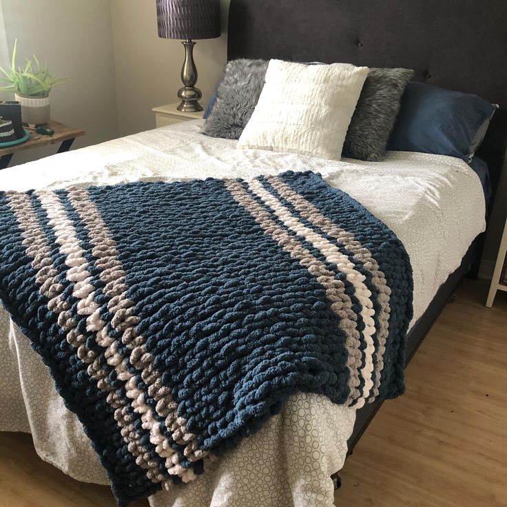 a bed with a blue and white blanket on it's headboard next to a night stand