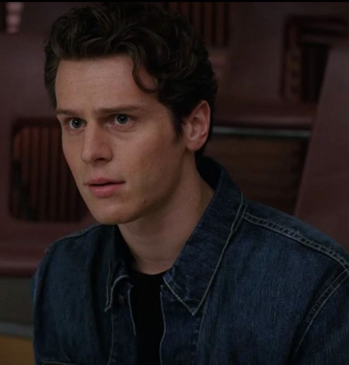 the young man is looking at something in the distance while wearing a denim shirt and jeans