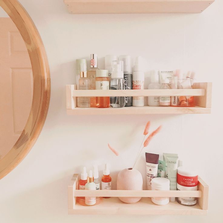 two wooden shelves filled with cosmetics and personal care items in front of a round mirror