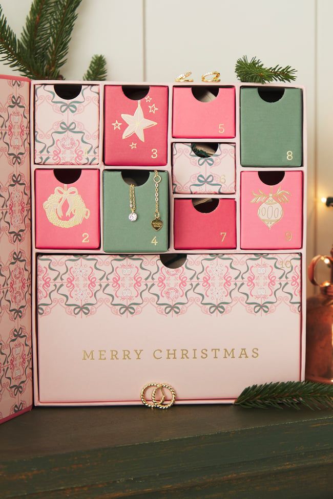 a pink and green christmas card holder on a table next to a pine tree with ornaments