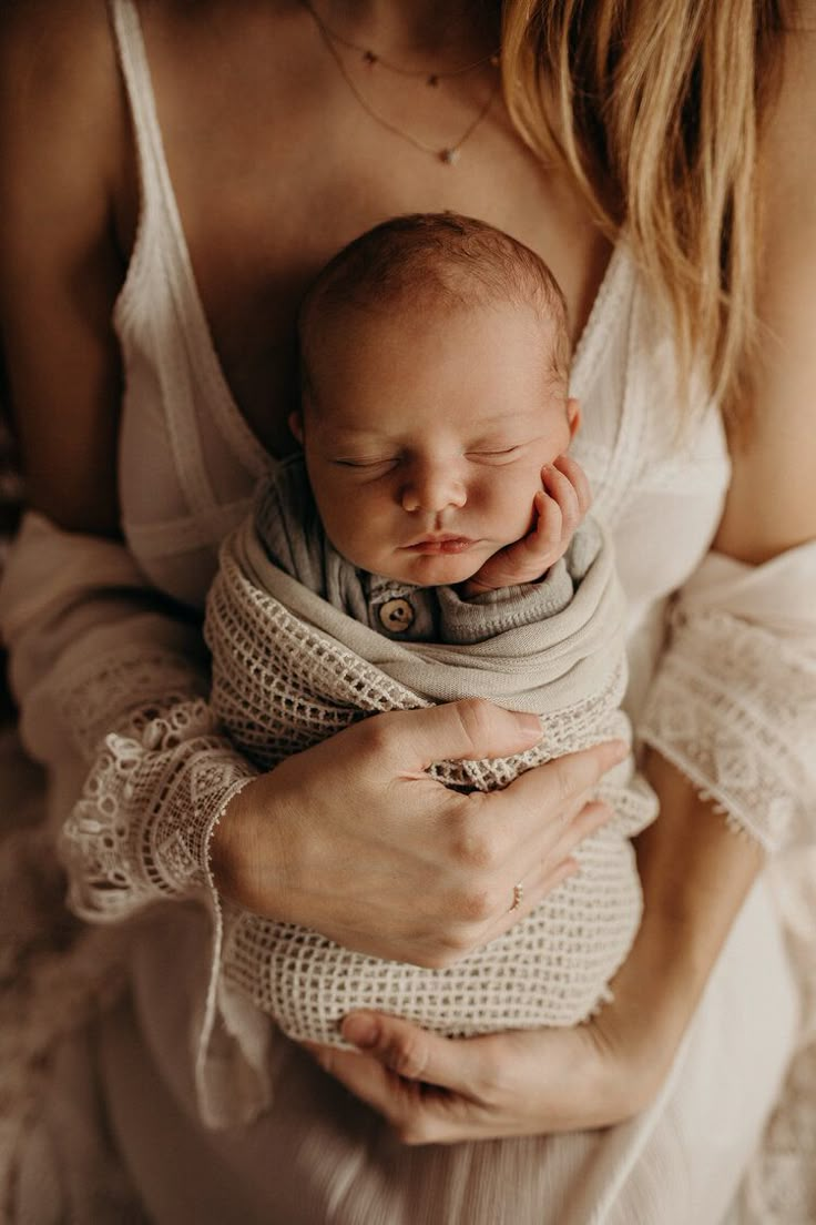 a woman holding a baby wrapped in a blanket while wearing a ring on her finger