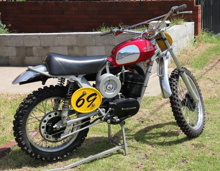 a red and black motorcycle parked on top of a grass covered field next to a brick wall