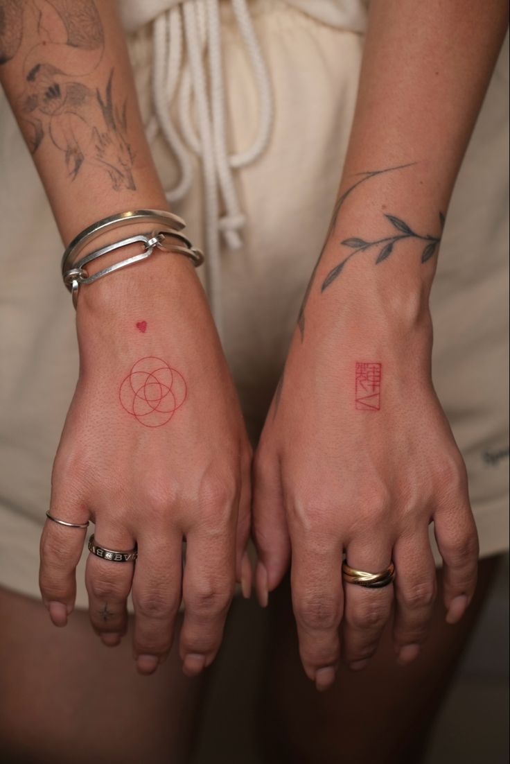 two people with tattoos on their hands holding each other's hands and looking at the camera