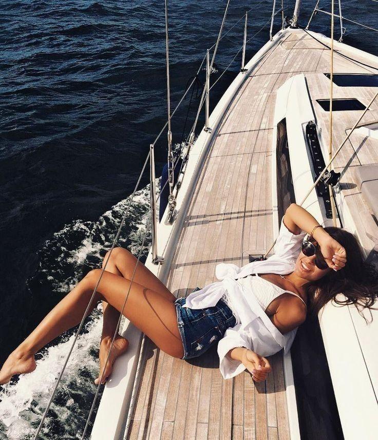 a beautiful woman laying on top of a boat next to the ocean with her legs spread out