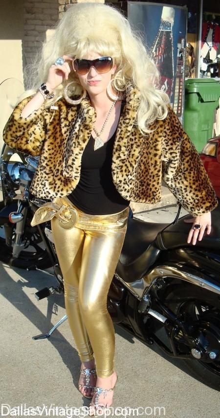 a woman with blonde hair wearing gold pants and leopard print jacket standing next to a motorcycle