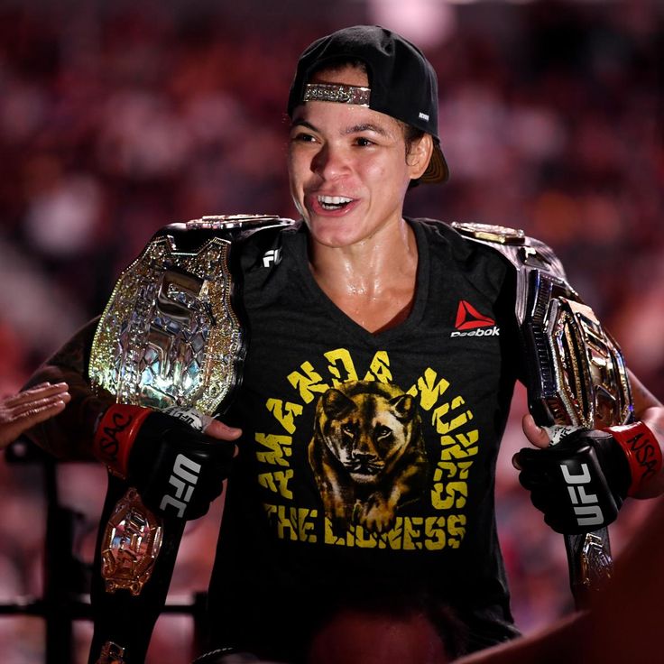 a woman in a black shirt and hat is holding two large belts while standing next to other people