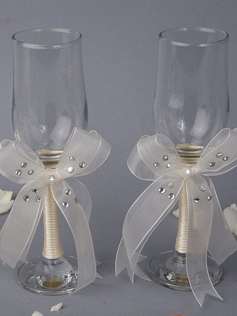 two wine glasses decorated with bows and pearls, one has a candle holder in the middle