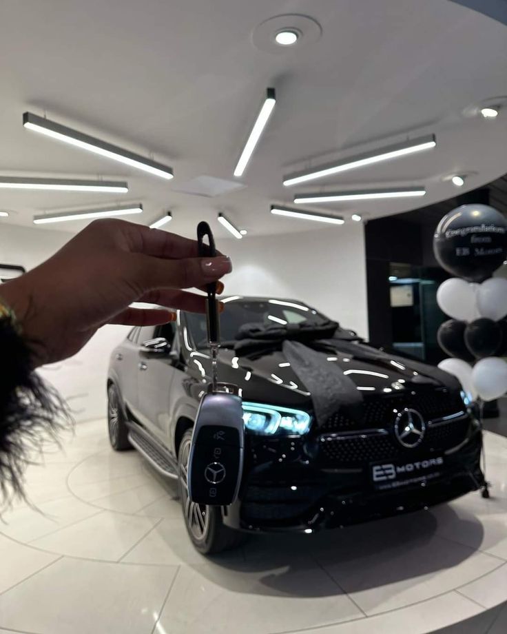 a person holding a key to a black car in a showroom filled with balloons