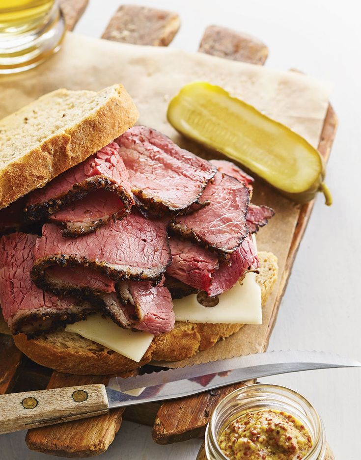 a corned beef sandwich with pickles and mustard on a cutting board next to it