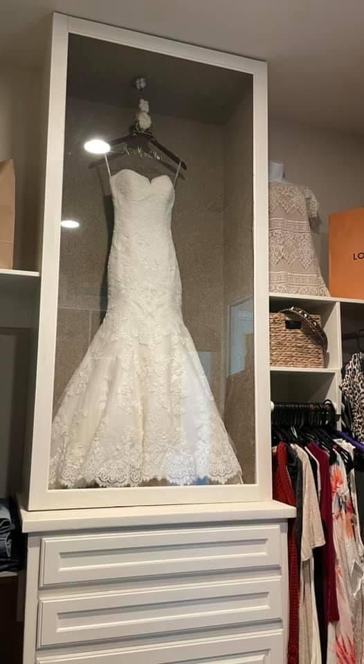 a wedding dress in a display case on top of a white shelf next to clothes