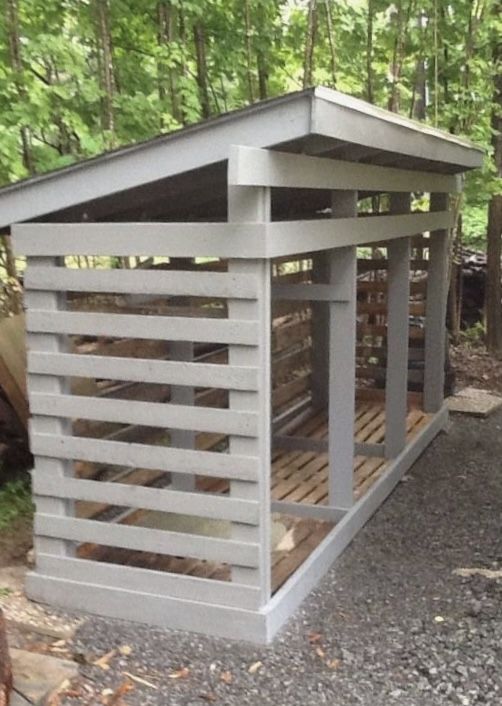 a small wooden shelter sitting in the middle of a forest next to a blue bucket