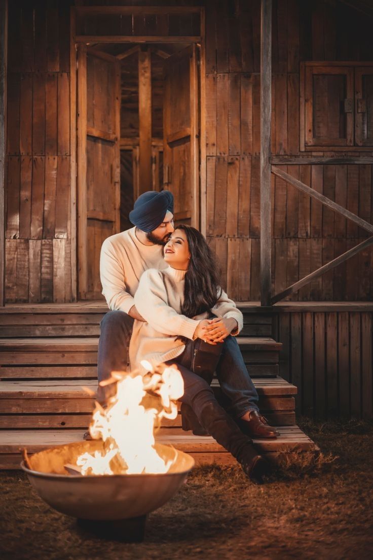 a man and woman sitting next to each other on a bench near a fire pit