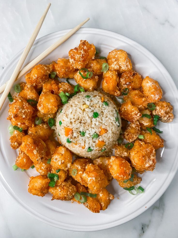 a white plate topped with chicken and rice next to chopsticks on a table